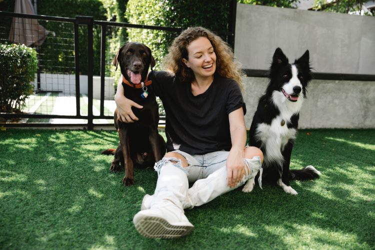 A happy pet owner sits between two dogs on a lawn.