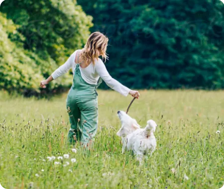 Une femme propriétaire d’animal de compagnie avec une assurance pour animaux de compagnie abordable jouant avec leur chien blanc dans un champ vert.