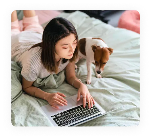 Femme allongée sur un lit regardant un ordinateur portable avec un chien terrier à ses côtés.